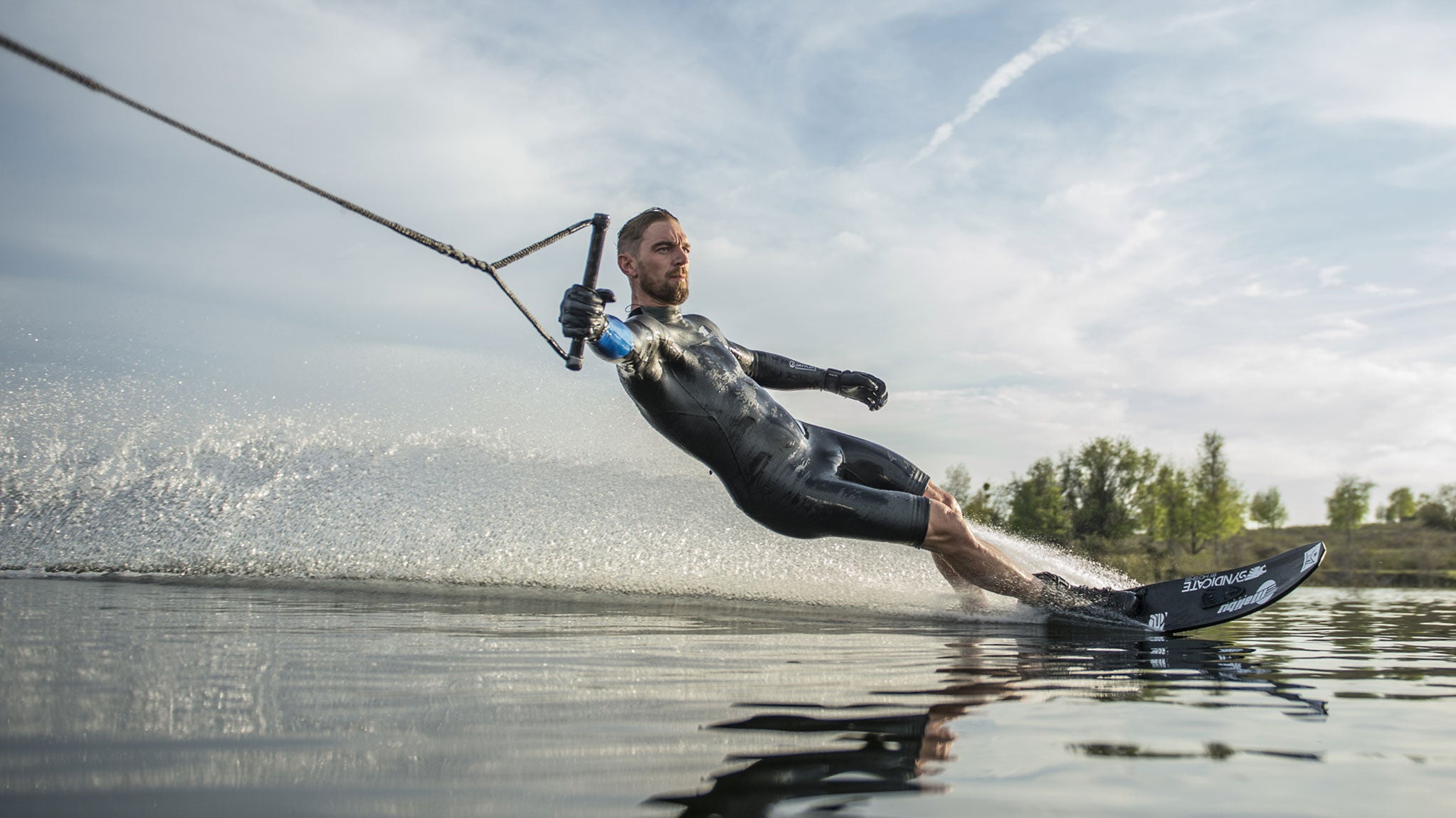 Water Skier turning with a one hand hold, wearing a black HO Sports Wetsuit and Gloves.