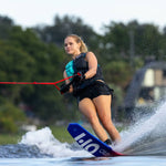 A waterskier carving through the water on the Omni Ultra White waterski, creating a spray while holding a red tow rope.
