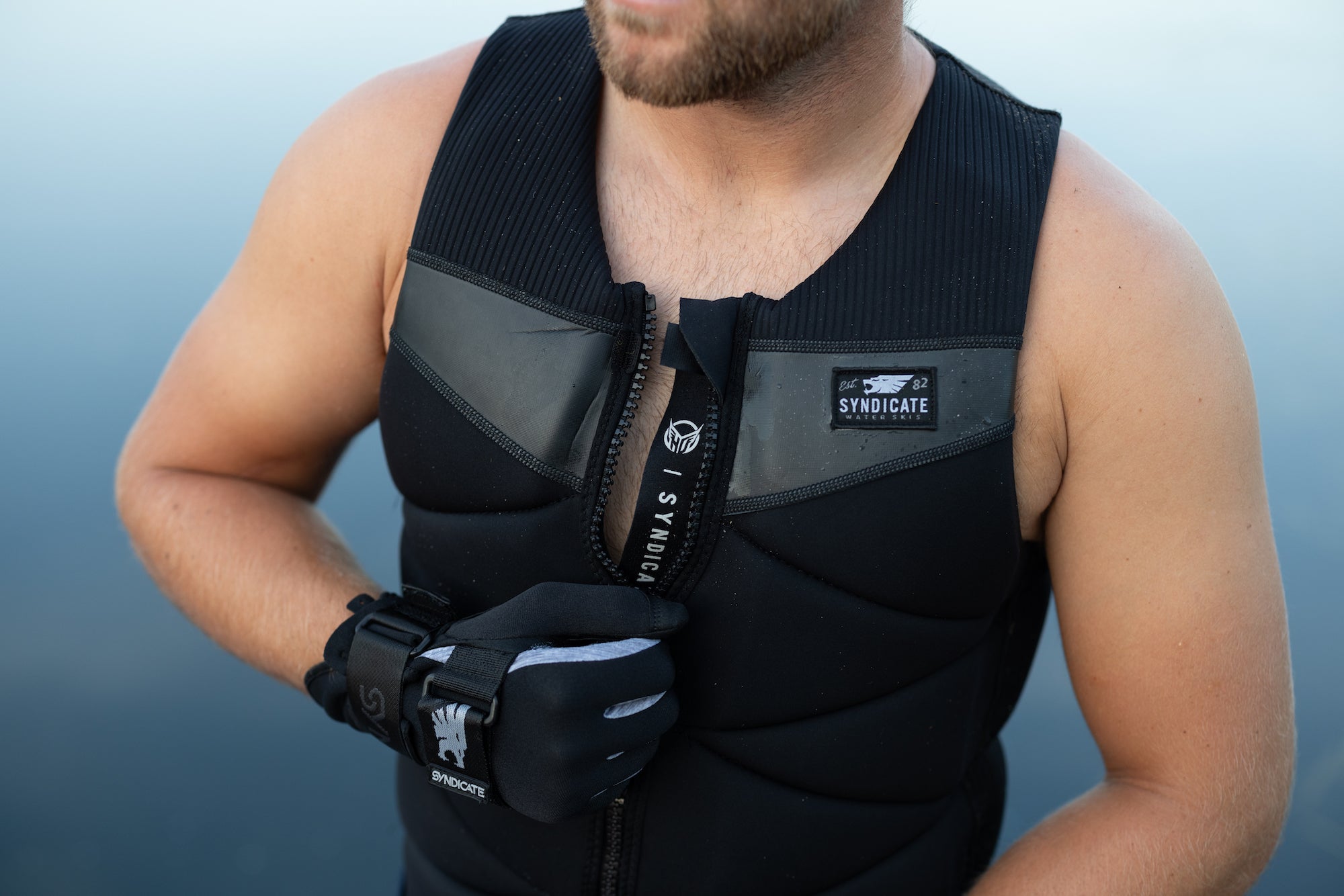 Close-up of a person wearing a black HO Sports Syndicate life vest and gloves near the water.