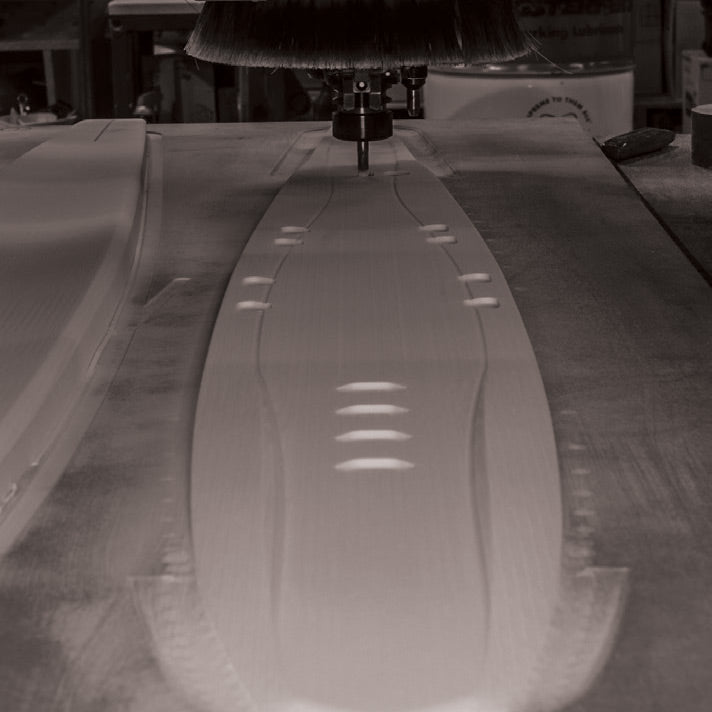 CNC machine shaping a wooden ski core with precise cutouts and smooth contours.