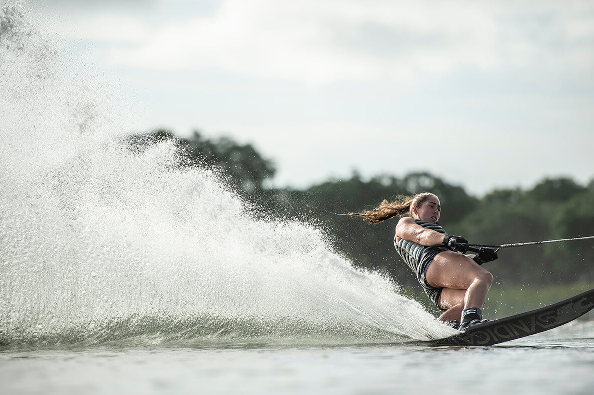 Female skier in a black vest cuts hard turn on a Syndicate ski with a powerful water spray.