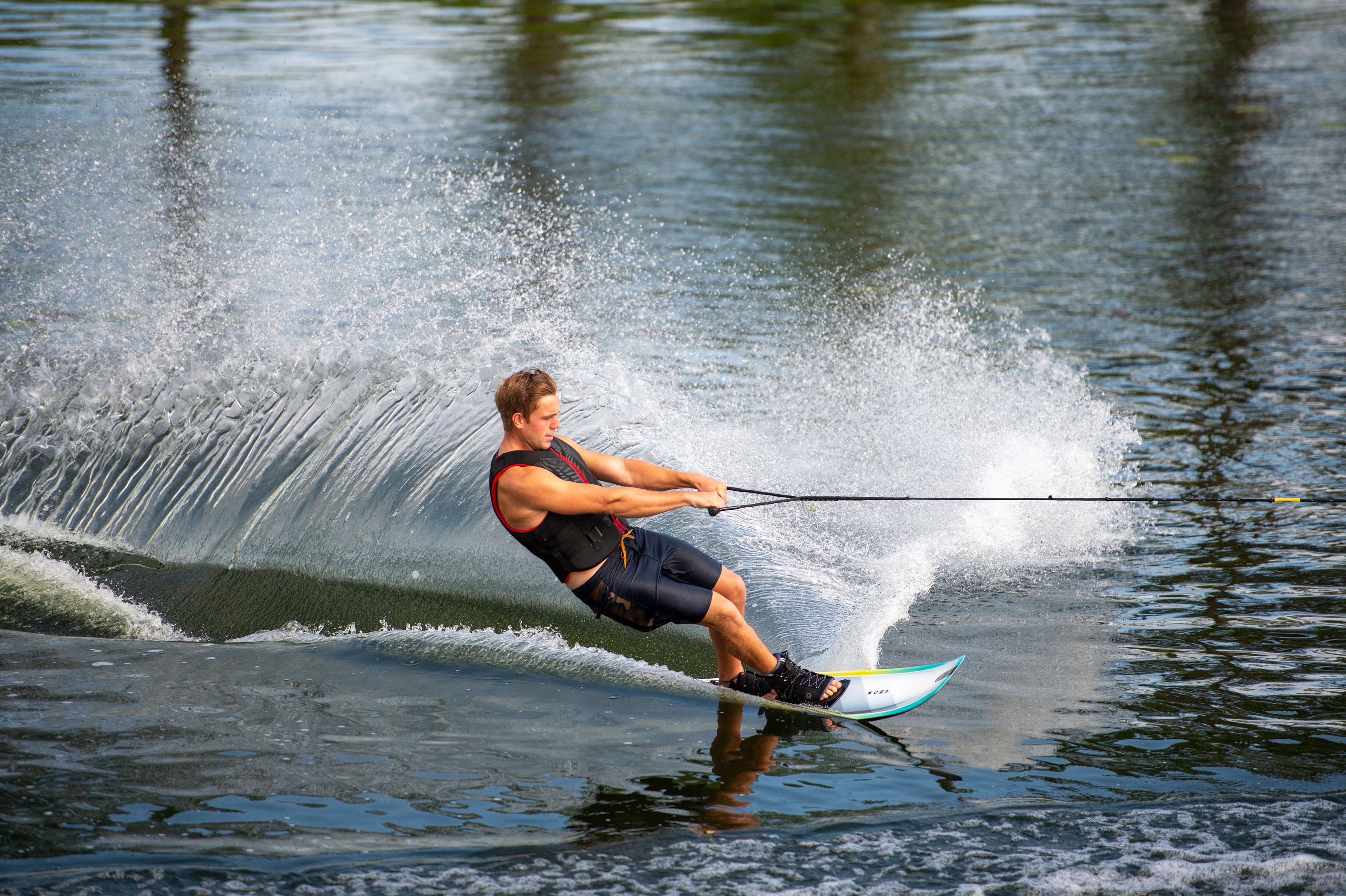 Man cutting hard on a slalom ski, sending up a wall of water.