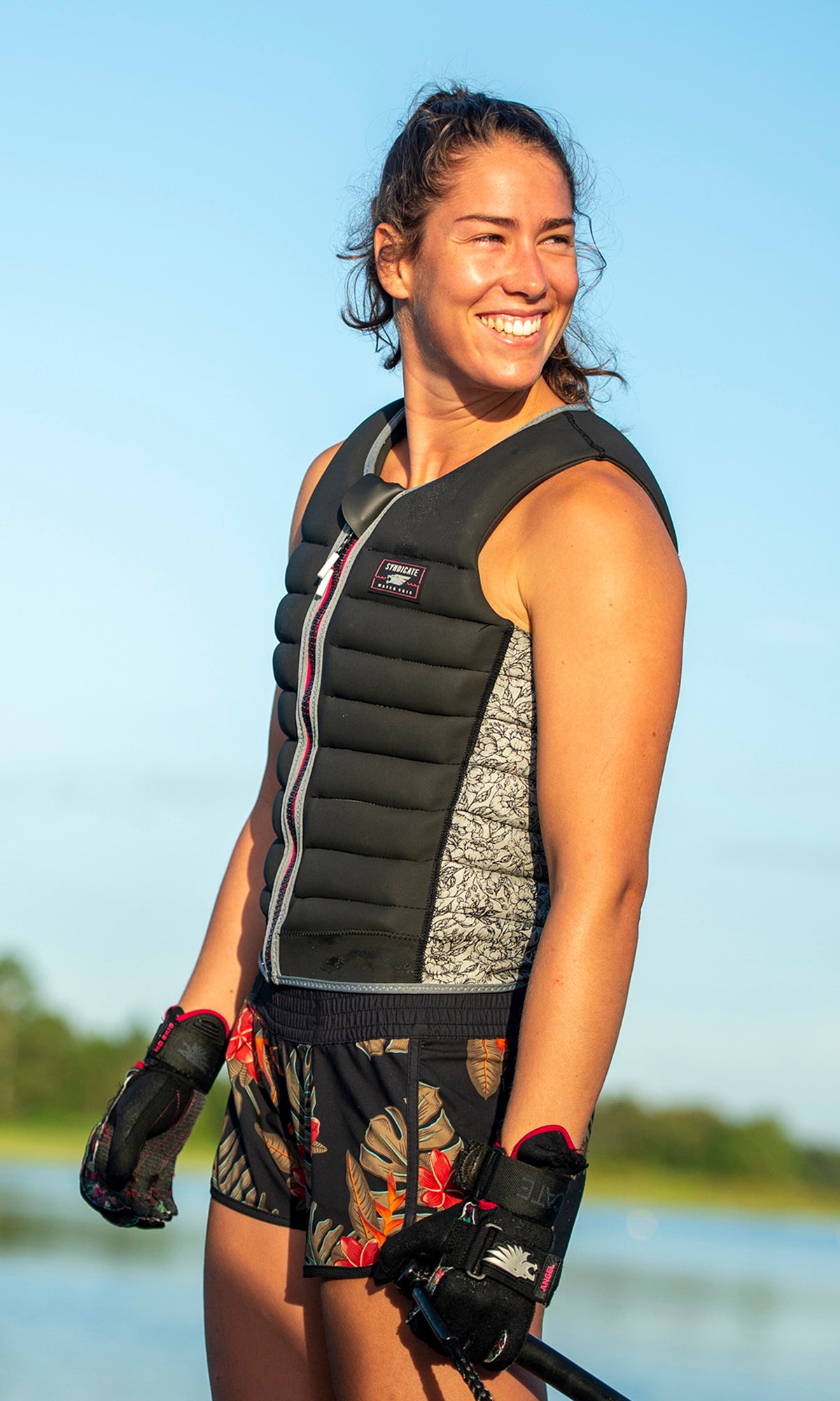 Smiling woman in black vest and floral shorts holds a rope handle, ready to ski.