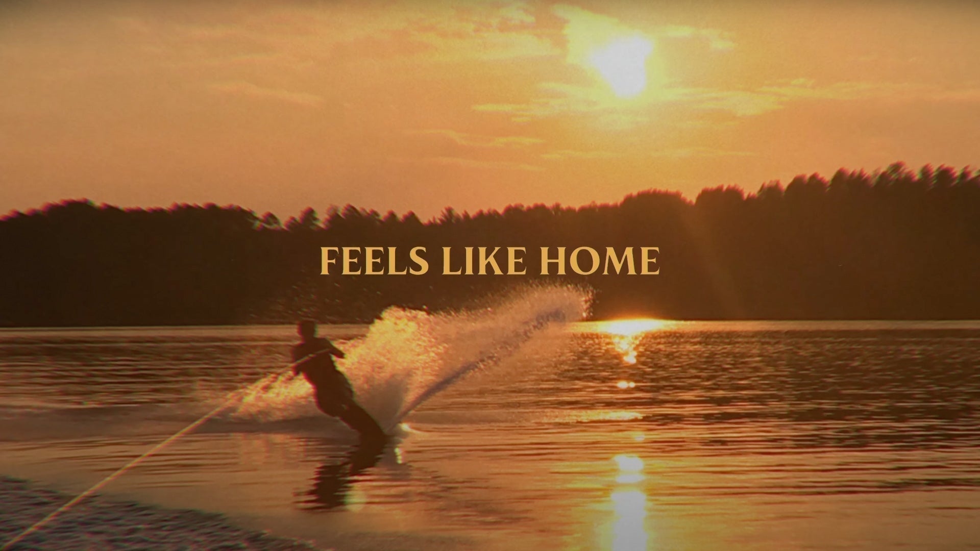 Waterskier carving at sunset on a calm lake with “Feels Like Home” text overlaid.