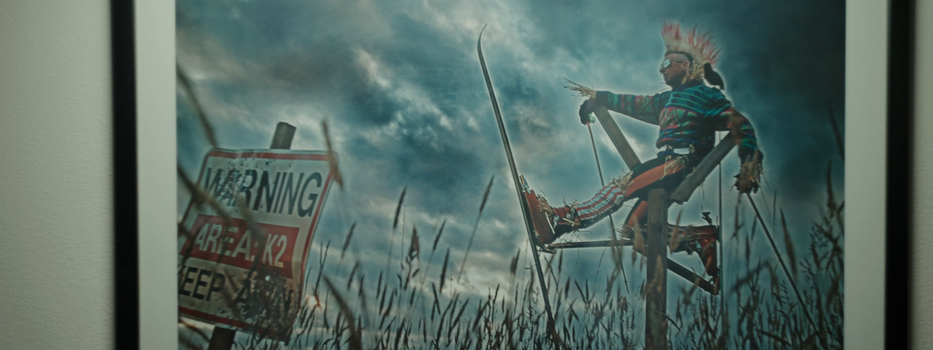 Skier in colorful costume balances on tall stilts near a warning sign in a grassy field.