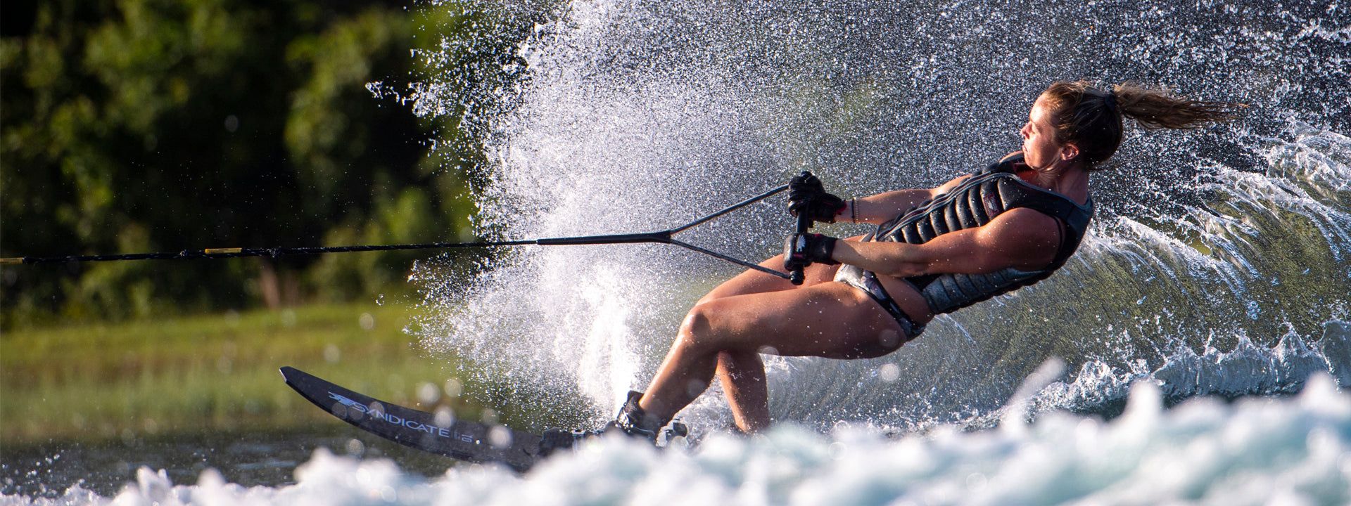 Allie Nicholson leans back on an HO Syndicate ski, carving through the water with a large spray behind her.