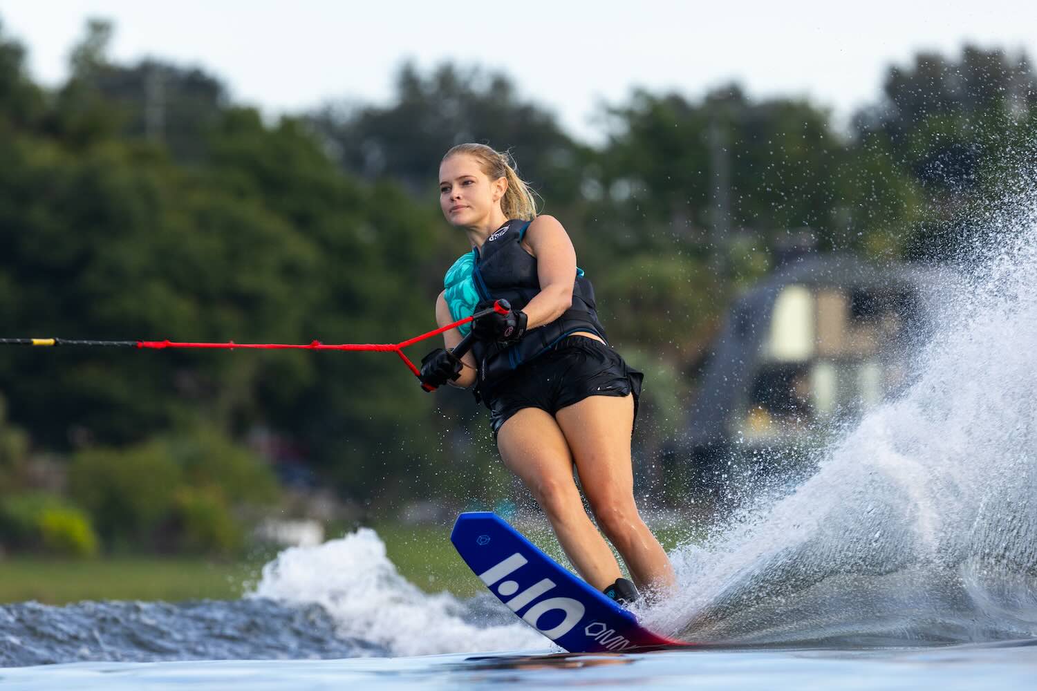 A waterskier carving through the water on the Omni Ultra White waterski, creating a spray while holding a red tow rope.