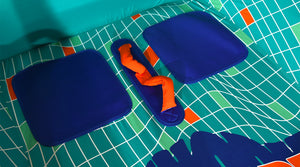 Close-up of blue seat panels flanking an orange grab handle on the teal grid-patterned deck.