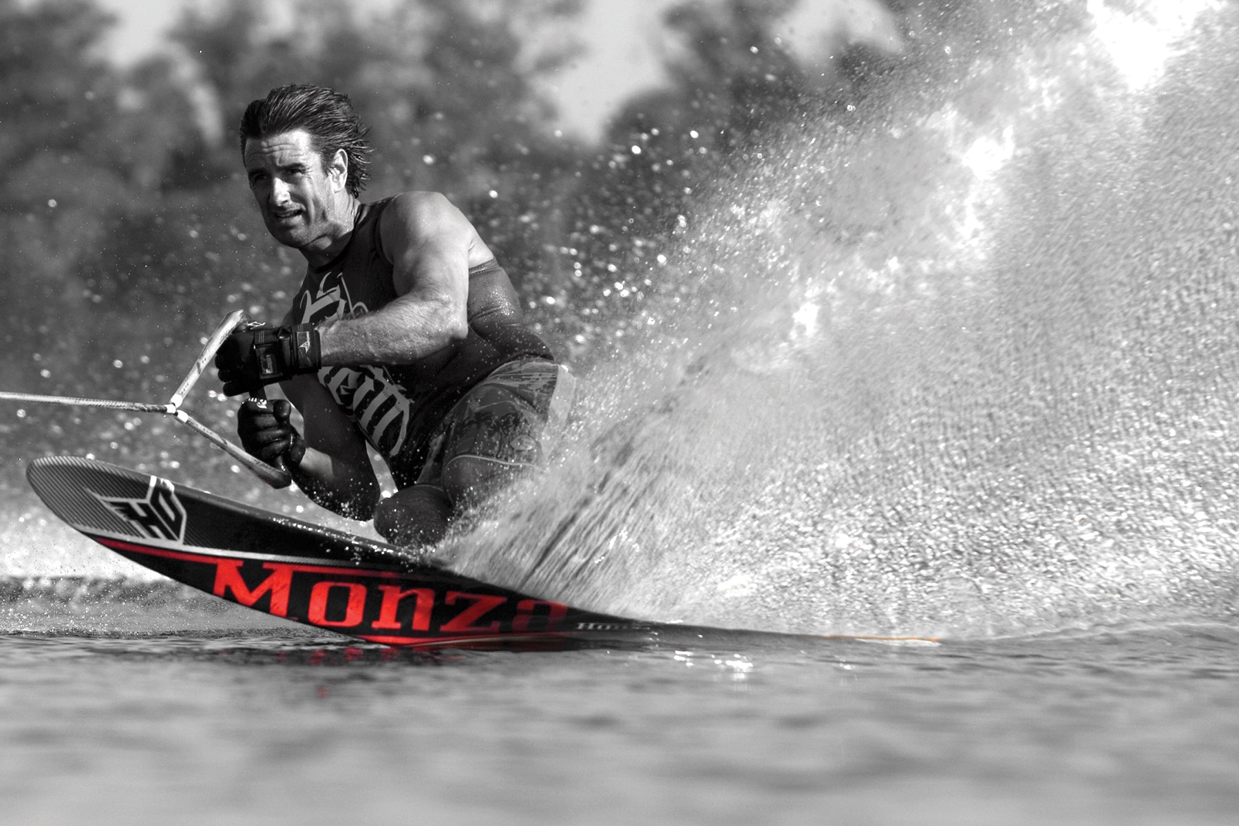 Black and white image of Wade Cox cutting through the water on a Monza ski, with selective color highlighting the red text.