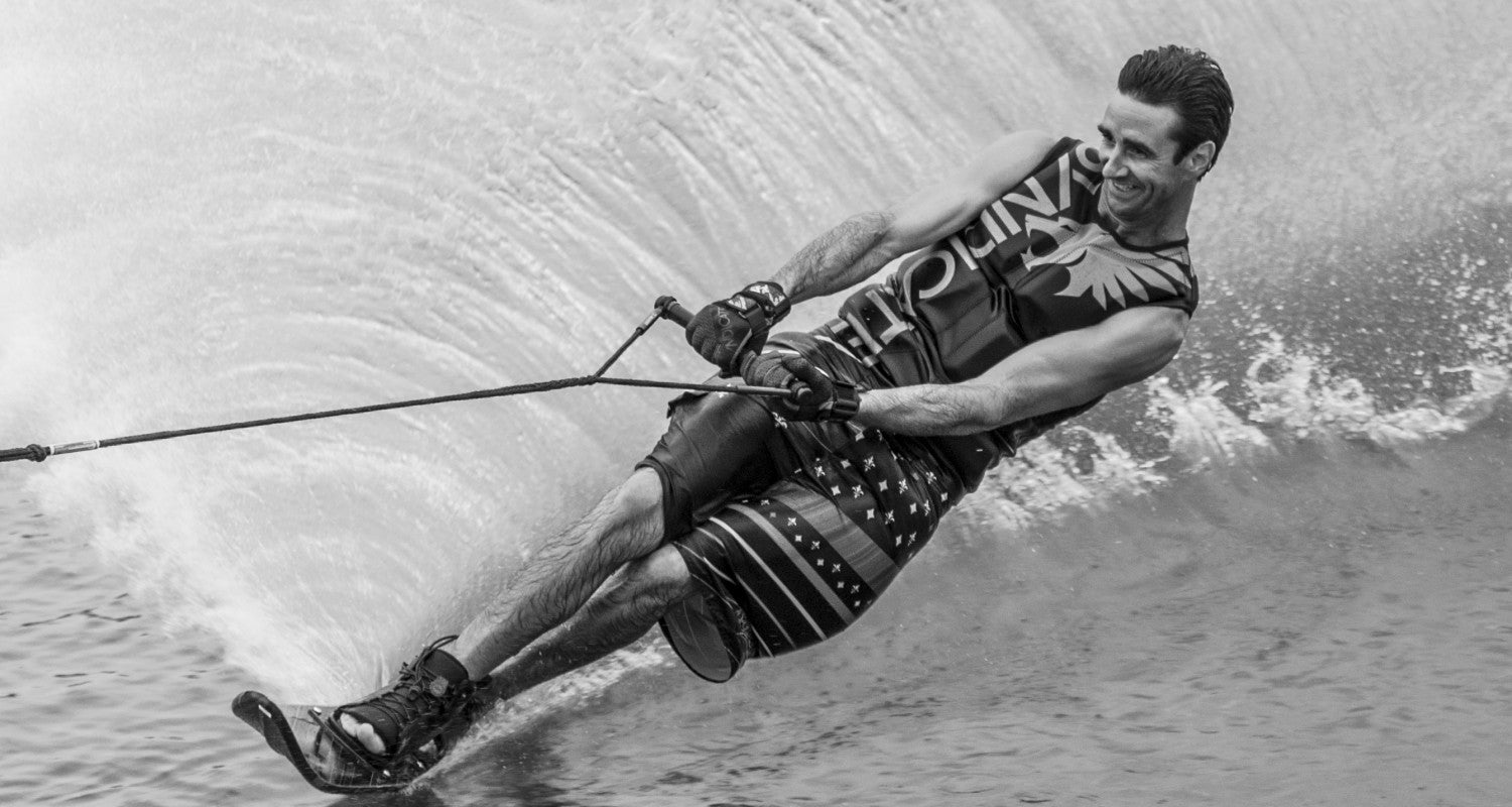 Black and white action shot of Wade Cox slalom water skiing, leaning sharply and cutting through the water.