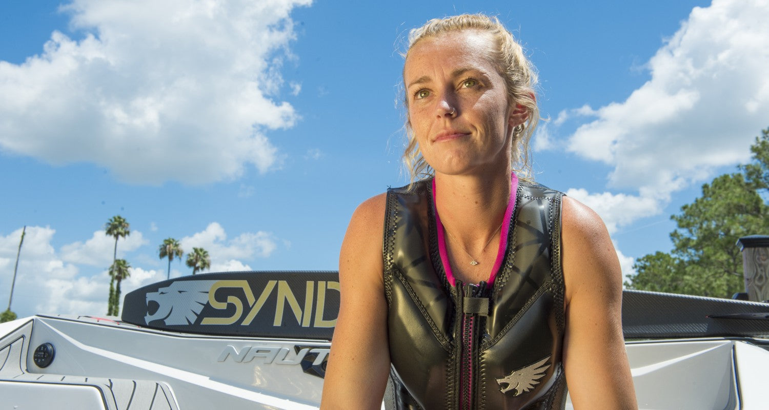 Allie Nicholson sits near a boat wearing a black HO Syndicate life vest with pink trim, looking into the distance.