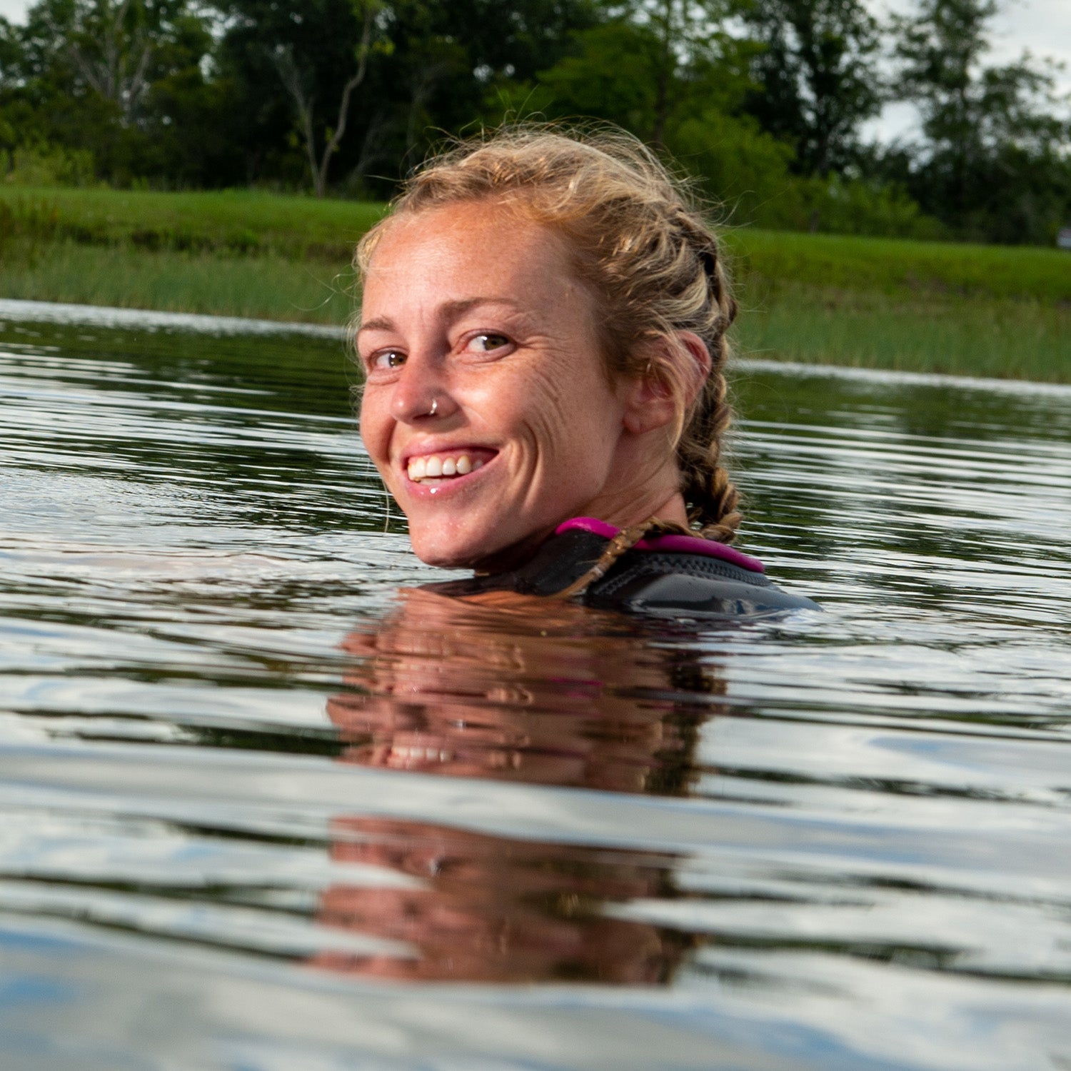 Allie Nicholson smiles while partially submerged in the water, wearing a black life vest with pink trim.