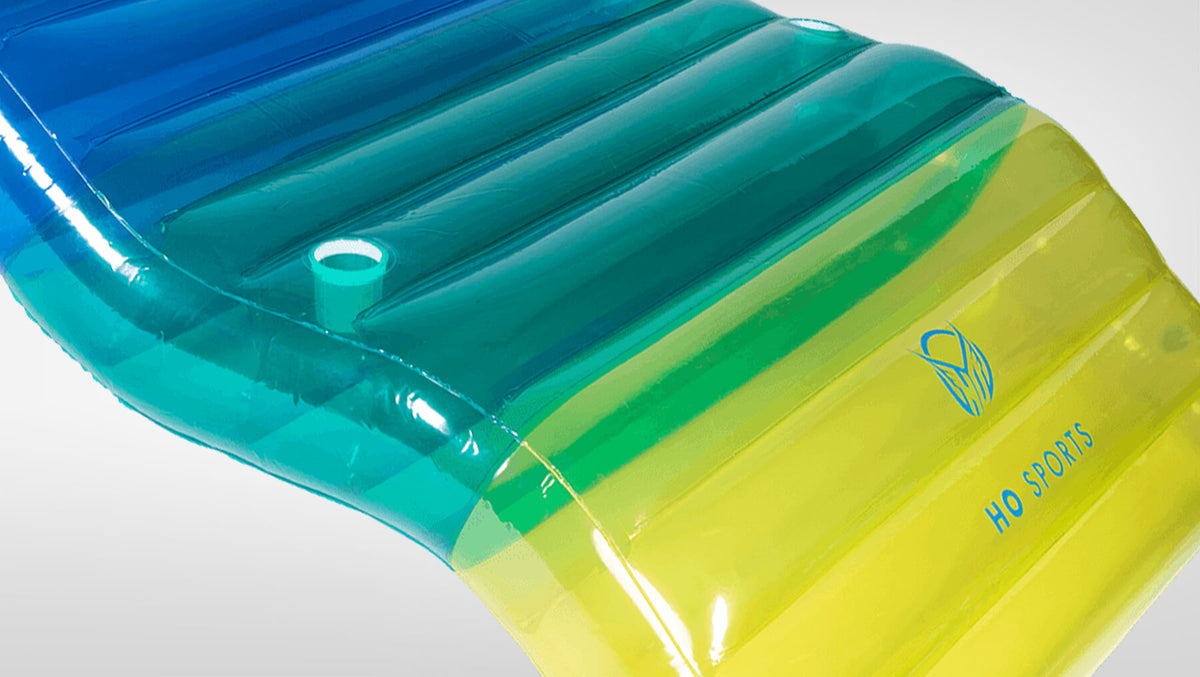 Angled view of Chaise Multi-Lounger's blue to yellow-green gradient surface with cup holder and HO Sports logo.