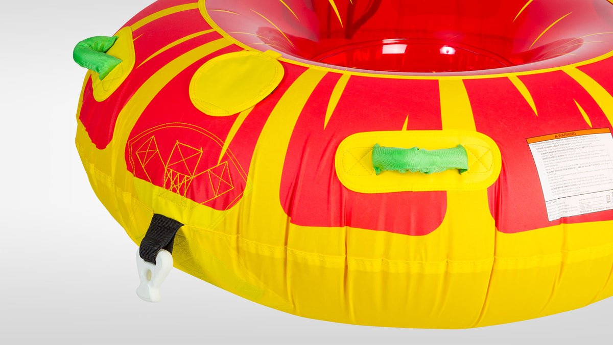 Angled view of Citrus Tube's red and yellow surface with green handles, tow strap, and warning label.