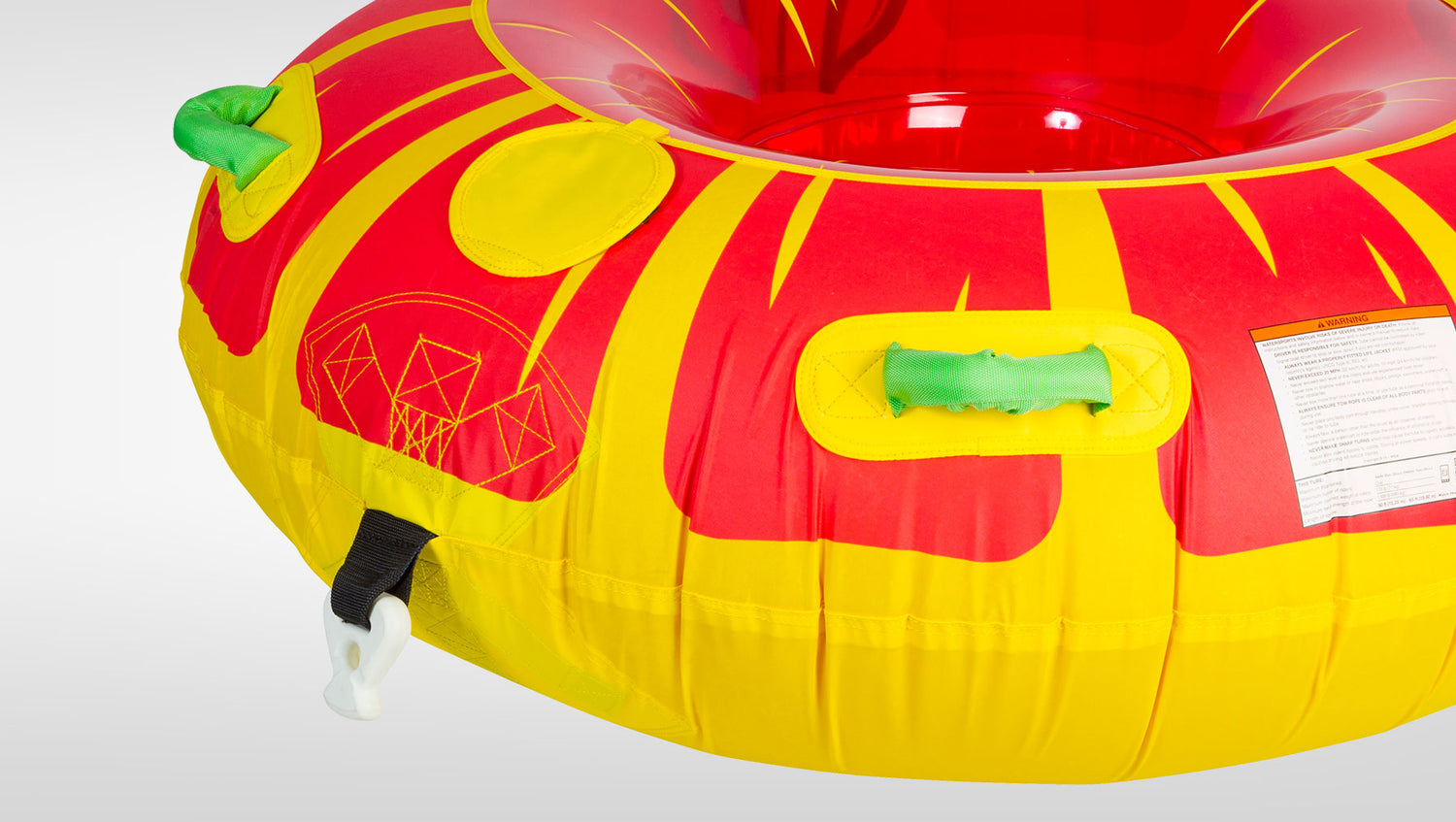 Angled view of Citrus Tube's red and yellow surface with green handles, tow strap, and warning label.